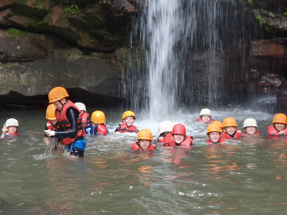students swi,ming in a waterfall wearing lifejackets and hard hats