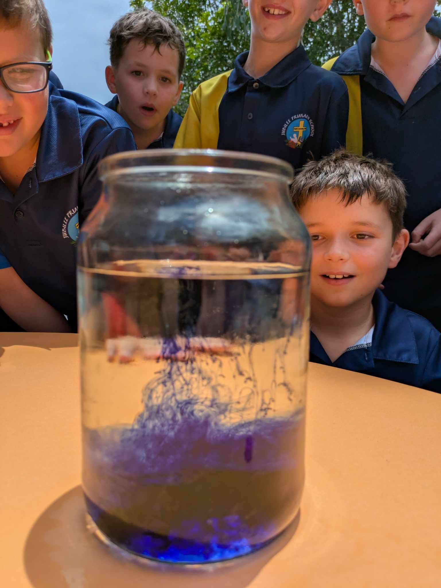 students surrounding a jar watching ink and water combine in a science experiment