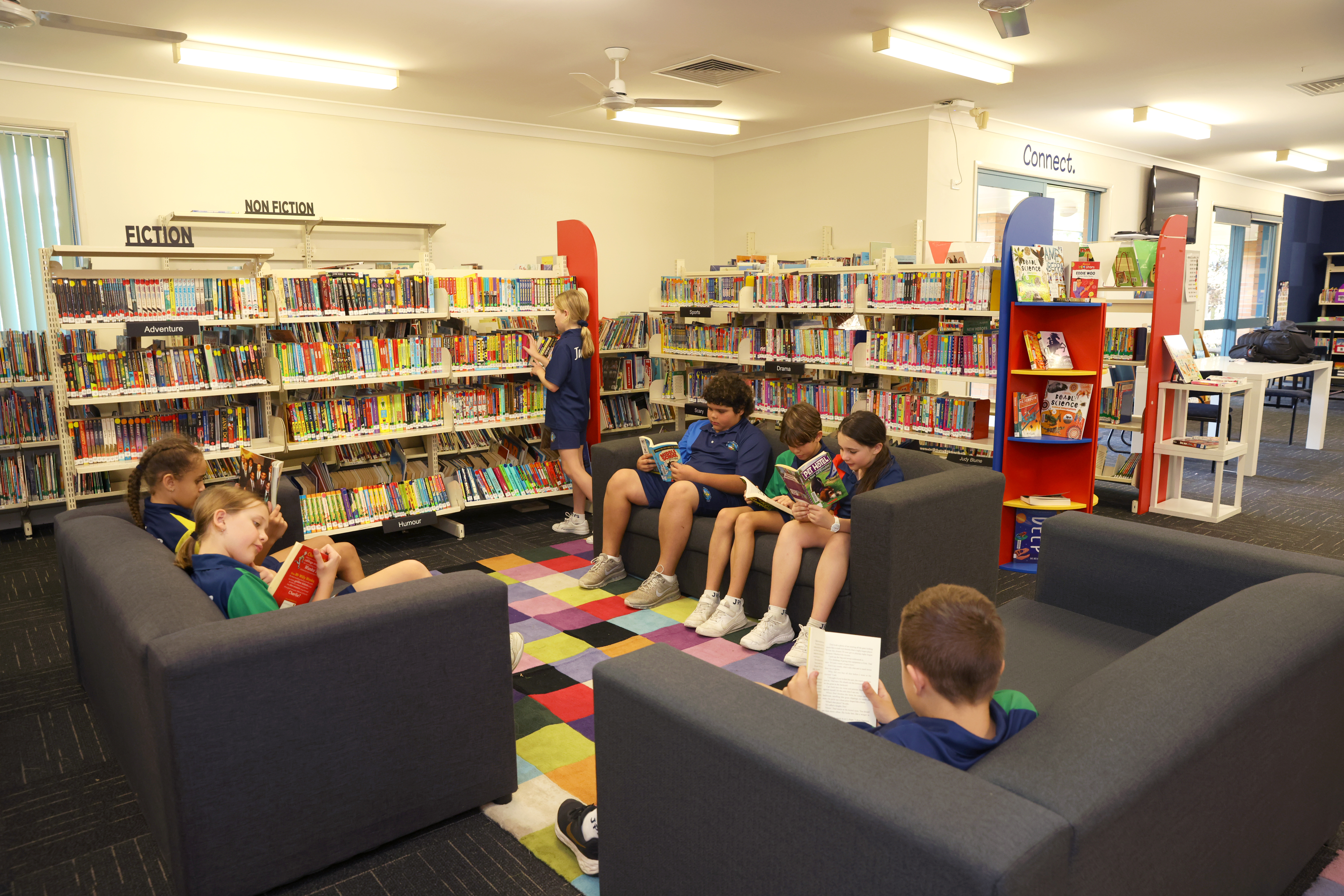 Students reading independently and browsing books in a school library with shelves organised into fiction and non fiction sections