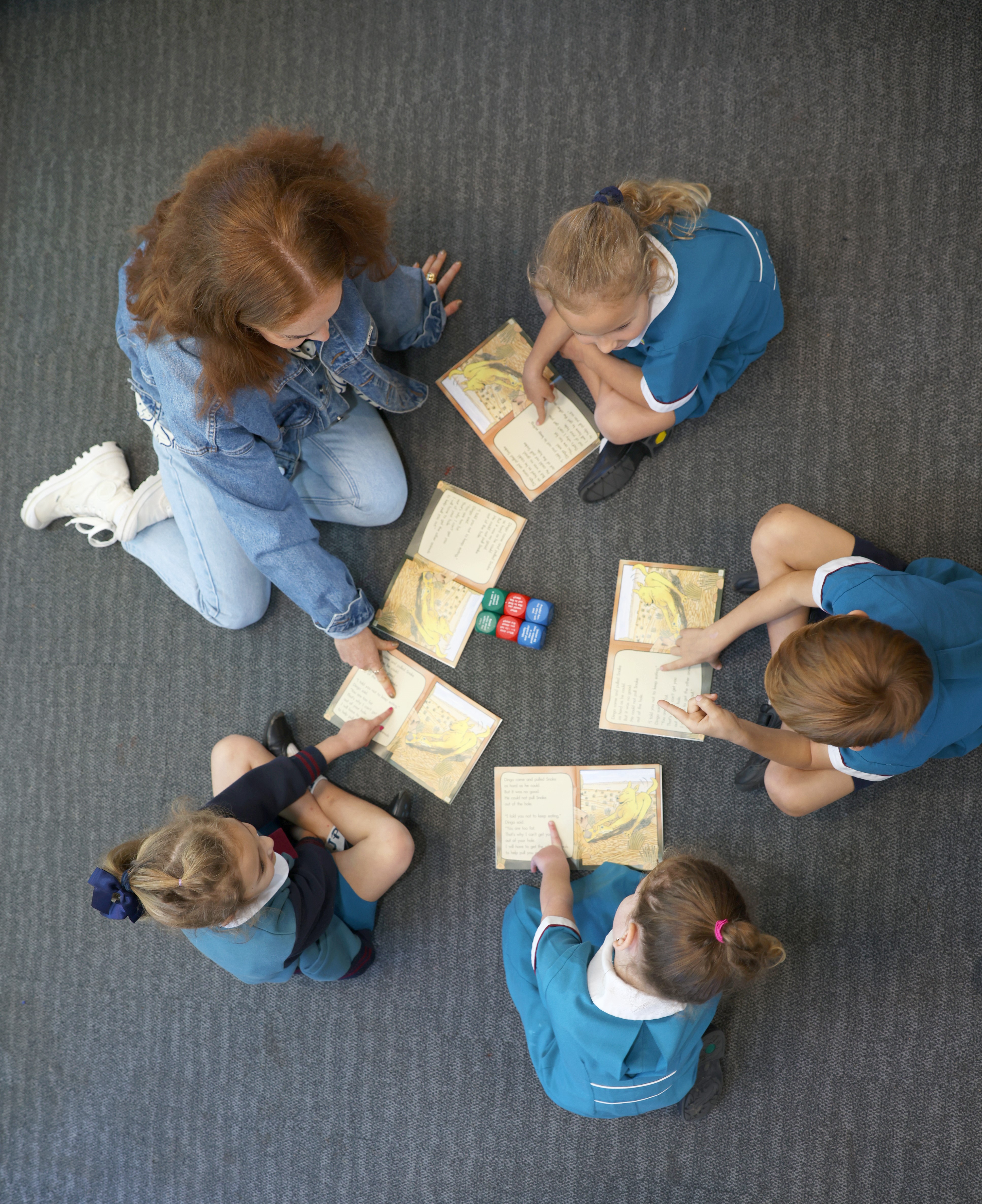 students and teacher sitting on floor reading a book in class