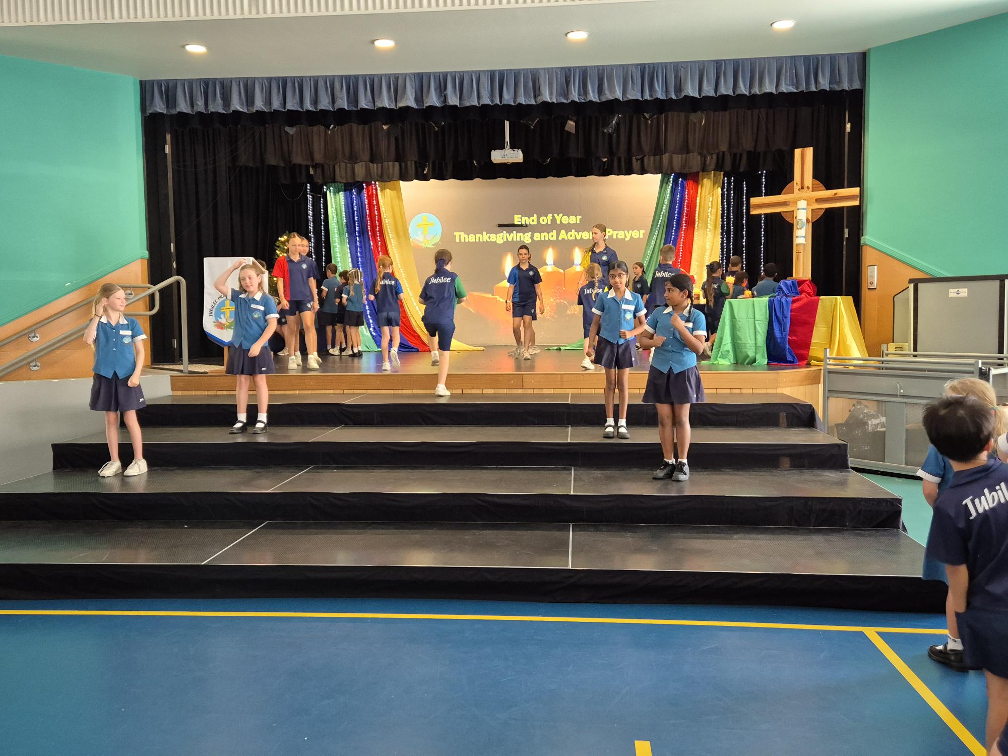 students standing on stage at end of year liturgy using the hall space to perform prayer 
