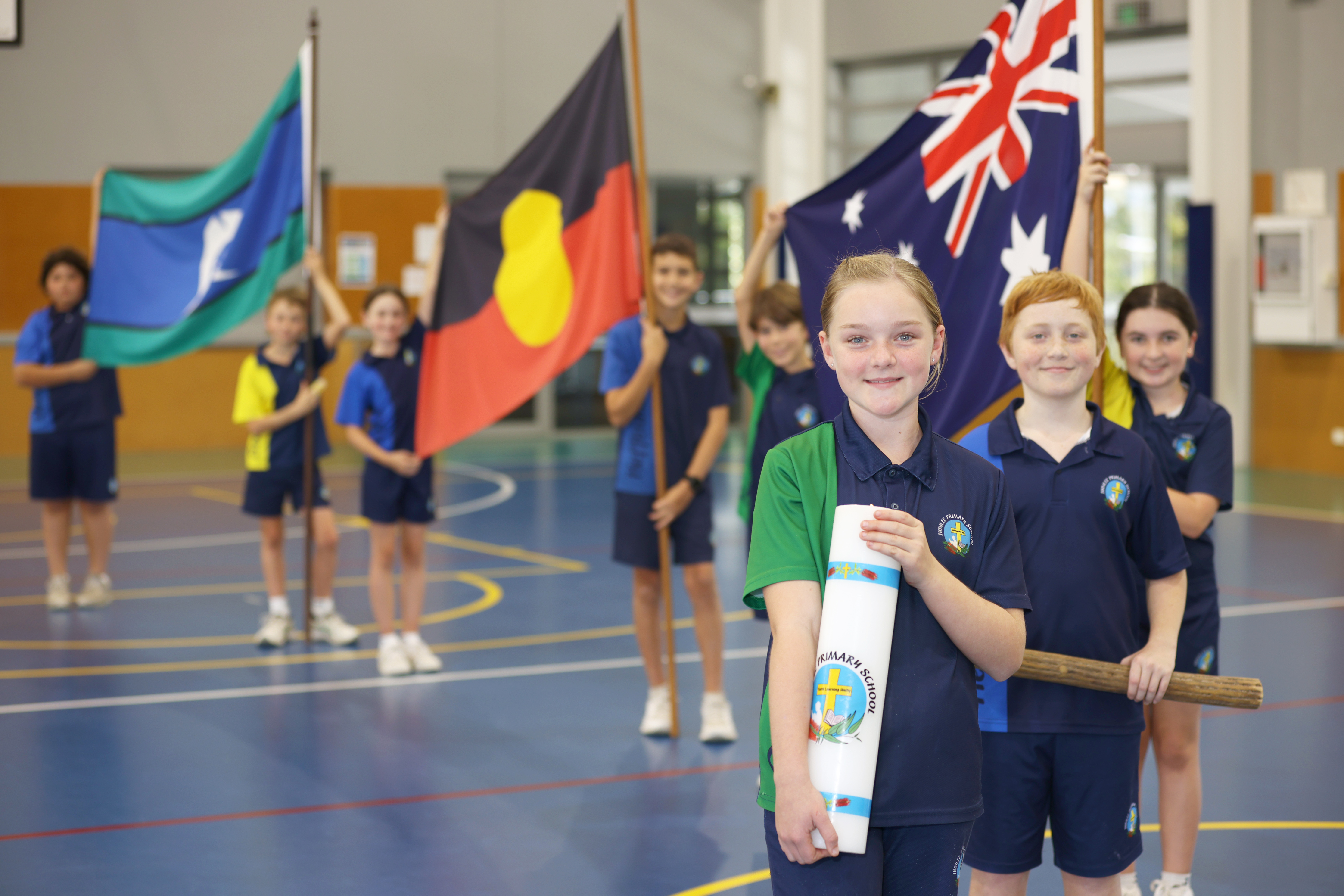Students seated at desks in a classroom using laptops for learning, wearing school uniforms, with classroom displays visible in 